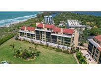 Beautiful aerial view of beachfront condo building with lush lawn, tropical landscaping, and close proximity to the beach at 8710 Midnight Pass Rd # 202, Sarasota, FL 34242