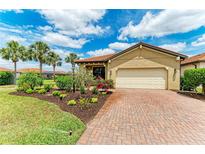 Inviting home with a brick driveway, two-car garage, lush landscaping, and beautiful palm trees against a bright sky at 10111 Malachite Dr, Bradenton, FL 34211