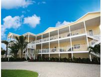 Multi-story yellow building with white railings, staircases, and mature palm trees at 1020 Sun N Sea Dr # 104B, Sarasota, FL 34242
