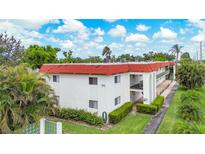 Low angle of a two-story condo complex with a red roof and lush, green landscaping on a bright, sunny day at 3500 Beneva Rd # 306, Sarasota, FL 34232