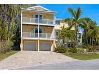 Charming yellow two-story home featuring double balconies, two-car garage, and lush tropical landscaping at 306 Poinsettia Rd, Anna Maria, FL 34216