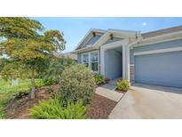 Charming home featuring a blue exterior, attached garage, and beautifully landscaped front yard with mature trees and flowering bushes at 8110 Trimbelle Ter, Parrish, FL 34219