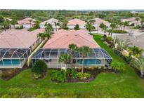 An aerial view of a tile-roofed home featuring a screened-in pool and lush, green landscaping in a tropical neighborhood at 6209 Erice St, Venice, FL 34293