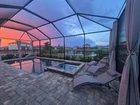 Beautiful pool area with lounge chairs inside a screened enclosure with a picturesque sunset view at 15719 Barefoot Beach Dr, Lakewood Ranch, FL 34211