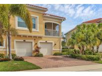 Inviting yellow townhouse featuring dual garages, red brick driveway, lush landscaping, and a charming second-story screened balcony at 4236 Expedition Way # 106, Osprey, FL 34229