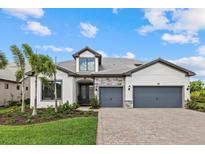 Charming two-story home with a two-car garage, stone accents, lush landscaping, and a brick paver driveway at 7765 Grande Shores Dr, Sarasota, FL 34240