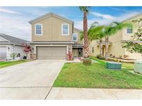 Two story home featuring a two-car garage, neutral stucco, manicured lawn and tropical landscaping with palm trees at 1912 Hawks View Dr, Ruskin, FL 33570