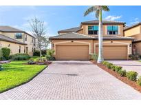 Well-maintained townhome showcasing a brick driveway, tropical landscaping, and a two-car garage at 6618 Grand Estuary Trl # 101, Bradenton, FL 34212