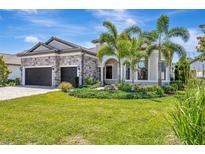 Elegant single-Gathering home featuring stone accents, a three-car garage, and lush tropical landscaping at 8033 Grande Shores Dr, Sarasota, FL 34240