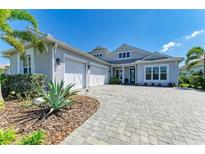 Beautiful gray home showcasing a three-car garage and a meticulously designed paver driveway at 8067 Waterbend Trl, Sarasota, FL 34240