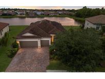 Beautiful waterfront home with a two-car garage and a brick driveway in a lush, landscaped neighborhood at 3512 Scrub Creek Run, Lakewood Ranch, FL 34211