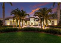 Stately Mediterranean-style home with manicured landscaping, palm trees, and a circular driveway at dusk at 7011 Belmont Ct, Lakewood Ranch, FL 34202