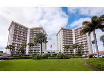 Bright, multi-story building complex with lush landscaping, palm trees, and an American flag under a blue sky at 2301 Gulf Of Mexico Dr # 36N, Longboat Key, FL 34228