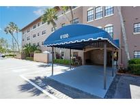 Attractive condo building entrance with blue awning for covered parking and tropical landscaping at 6100 Gulfport S Blvd # 117, Gulfport, FL 33707