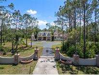 Lovely home exterior with a circular driveway and gated entrance, surrounded by mature trees and blue skies at 21616 67Th E Ave, Bradenton, FL 34211