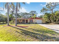 Charming single-story home with well-manicured lawn, mature palm trees, and attached one-car garage at 1621 Overbrook Rd, Englewood, FL 34223