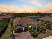 Stunning aerial view of a tile-roof home featuring a brick driveway and a serene lake backdrop at sunset at 20655 Valprato Ct, Venice, FL 34293