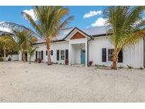 Charming two-story home featuring a white exterior, a blue front door, and lush palm trees in the front yard at 305 73Rd St, Holmes Beach, FL 34217