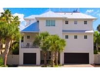 Beautiful, modern two story home with white exterior, dark garage doors and lush tropical landscaping at 205 17Th N St, Bradenton Beach, FL 34217