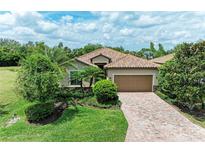 Beautiful single-story home featuring a terracotta-tiled roof, paver driveway, and lush tropical landscaping at 157 Wandering Wetlands Cir, Bradenton, FL 34212