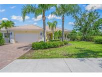 Charming home with lush landscaping, palm trees, a brick driveway, and a cream-colored exterior at 5821 Valente Pl, Sarasota, FL 34238