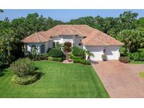 Elegant home with a red tile roof, lush landscaping, and a well-manicured lawn and brick paved driveway at 6612 Butlers Crest Dr, Bradenton, FL 34203