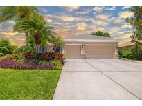 Charming home featuring a well-manicured lawn, lush tropical landscaping, and a spacious two-car garage at 7804 Edmonston Cir, University Park, FL 34201