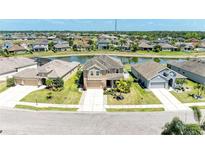 Aerial view of a tan two-story home on a pond with a well-manicured lawn and lush landscaping at 7822 110Th E Ave, Parrish, FL 34219