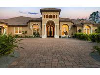 Close-up of a custom home with a grand arched entrance, terracotta roof, brick driveway, and manicured landscaping at 20706 79Th E Ave, Bradenton, FL 34202