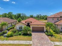 Beautiful single-Gathering home featuring a red-tiled roof, paver driveway, two-car garage, and lush tropical landscaping at 12315 Canavese Ln, Venice, FL 34293