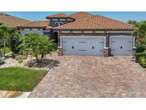 Beautiful home exterior featuring a three-car garage, a brick driveway and lush landscaping at 13786 Vancanza Dr, Venice, FL 34293