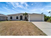 Charming single-story home featuring a two-car garage, arched windows, and tropical landscaping in the front yard at 11 Lateen Sail Dr, Placida, FL 33946