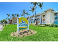 Exterior view of La Costa Condominiums with lush lawn and palm trees under a clear blue sky at 1800 Gulf N Dr # 112, Bradenton Beach, FL 34217
