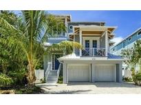 Charming two-story home with a two-car garage, beautiful landscaping, and a cozy balcony on a sunny day at 212 Spring Ave, Anna Maria, FL 34216