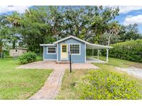 Charming blue home with a yellow door, brick walkway, covered parking, and lush landscaping at 3608 Water St, Ellenton, FL 34222