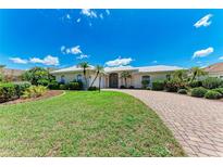 Charming single-story home with a brick driveway, lush green lawn, and beautiful landscaping at 585 Khyber Ln, Venice, FL 34293