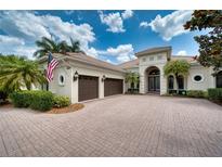 Inviting cream-colored home with a beautiful tile roof, arched entryway, well-manicured landscaping, and spacious brick driveway at 6919 Dominion Ln, Lakewood Ranch, FL 34202