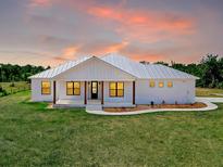 Charming single-story home with white siding, metal roof, and lush green lawn under a colorful sunset sky at 27510 67Th E Ave, Myakka City, FL 34251