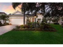 Charming single-story home featuring a manicured lawn, paver driveway, and lush landscaping with elegant exterior lighting at 13848 American Prairie Pl, Lakewood Ranch, FL 34211