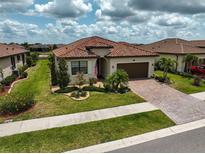 Charming home with a red tile roof, manicured lawn, and a brick paver driveway at 20542 Trattoria Loop, Venice, FL 34293
