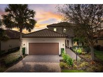 Charming two-story home with a brick driveway, lush landscaping, and warm exterior lighting at dusk at 12822 Del Corso Loop, Bradenton, FL 34211