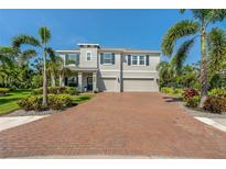 Charming two-story home with a three-car garage, brick driveway, lush landscaping, and beautiful palm trees at 5805 49Th E Ct, Ellenton, FL 34222