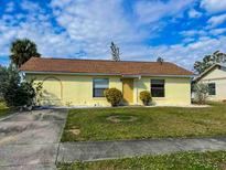 Charming single-story home with a yellow exterior, well-maintained lawn and a brown roof under a partly cloudy sky at 6113 Mckee St, Port Charlotte, FL 33981