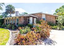 Charming single-story brick home featuring a well-maintained landscaped front yard with mature trees and vibrant flowering plants at 911 Cimarron Cir, Bradenton, FL 34209