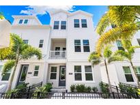 Charming three-story townhome with white siding, balcony, and lush tropical landscaping at 2408 Ezzell Ct, Sarasota, FL 34237