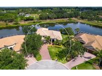 Stunning aerial view of waterfront home with brick driveway, lush landscaping, and private pool at 2496 Farms Ct, Sarasota, FL 34240