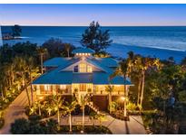 Stunning beachfront home with lush landscaping, palm trees, and breathtaking ocean views at twilight at 26 Sandy Hook S Rd, Sarasota, FL 34242