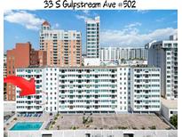 Condo building with pool and lounge chairs with building in sunny location at 33 S Gulfstream Ave # 502, Sarasota, FL 34236