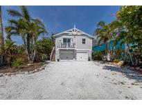Charming two-story home with a white gravel driveway, lush landscaping, and a light gray facade at 799 Jacaranda Rd, Anna Maria, FL 34216