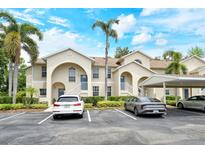 Beige two-story condo building featuring arched entryways, blue doors, well-maintained landscaping, and covered parking at 8315 Glenrose Way # 1421, Sarasota, FL 34238